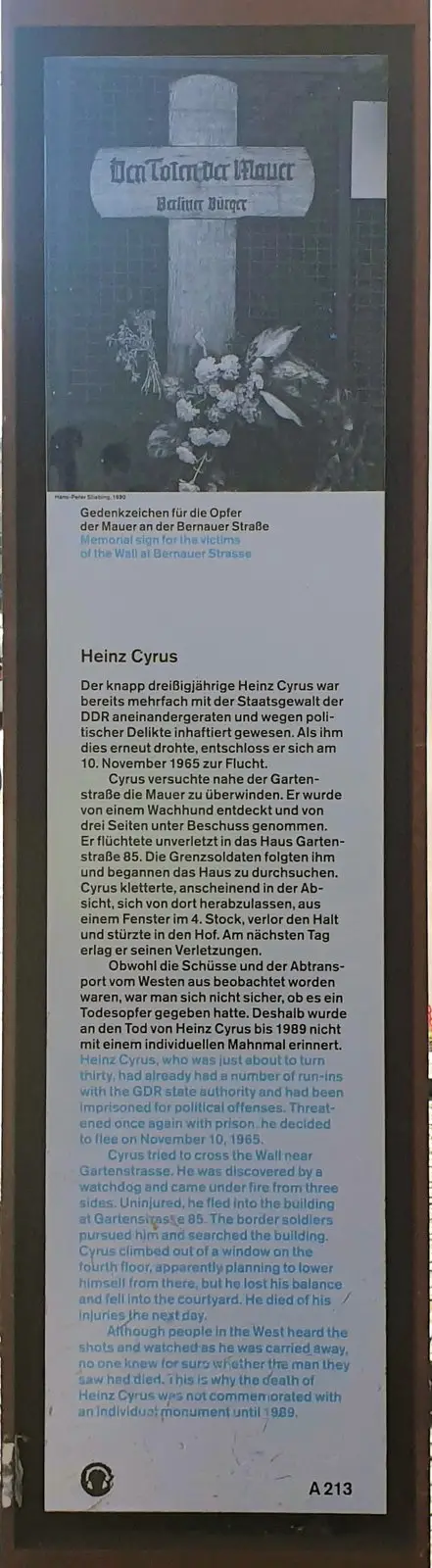 Tall panel with a black-and-white photograph of a wooden cross with flowers, above German and English text headed "Heinz Cyrus"
