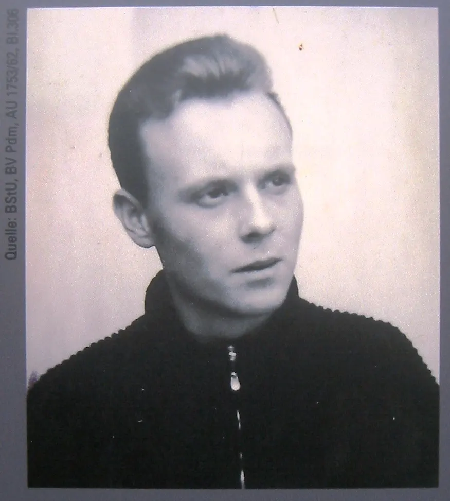 Black-and-white portrait of a young man with swept-back hair in a dark zip-up jacket