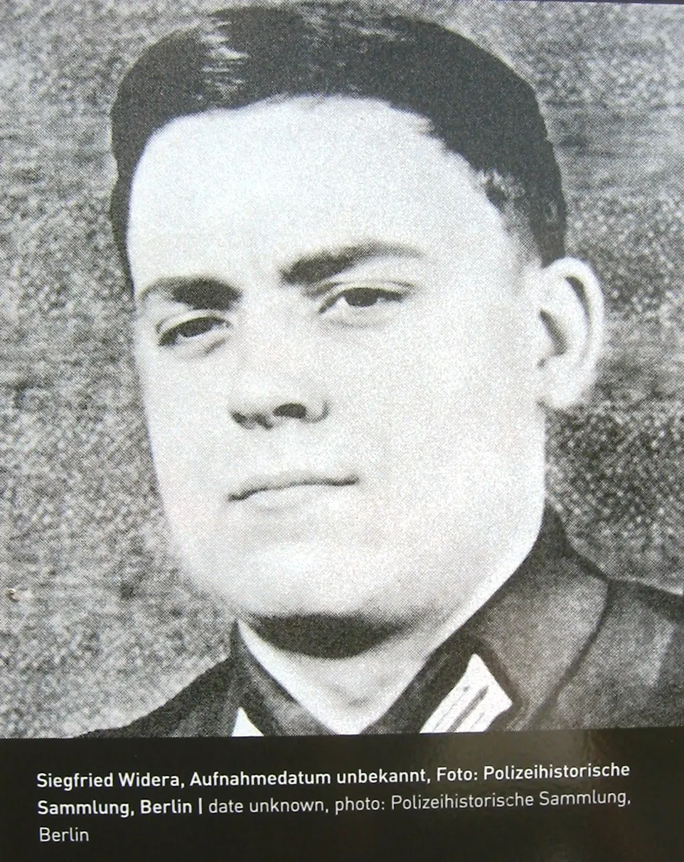 Black-and-white portrait of a young man with short dark hair in a uniform jacket, with a printed caption below