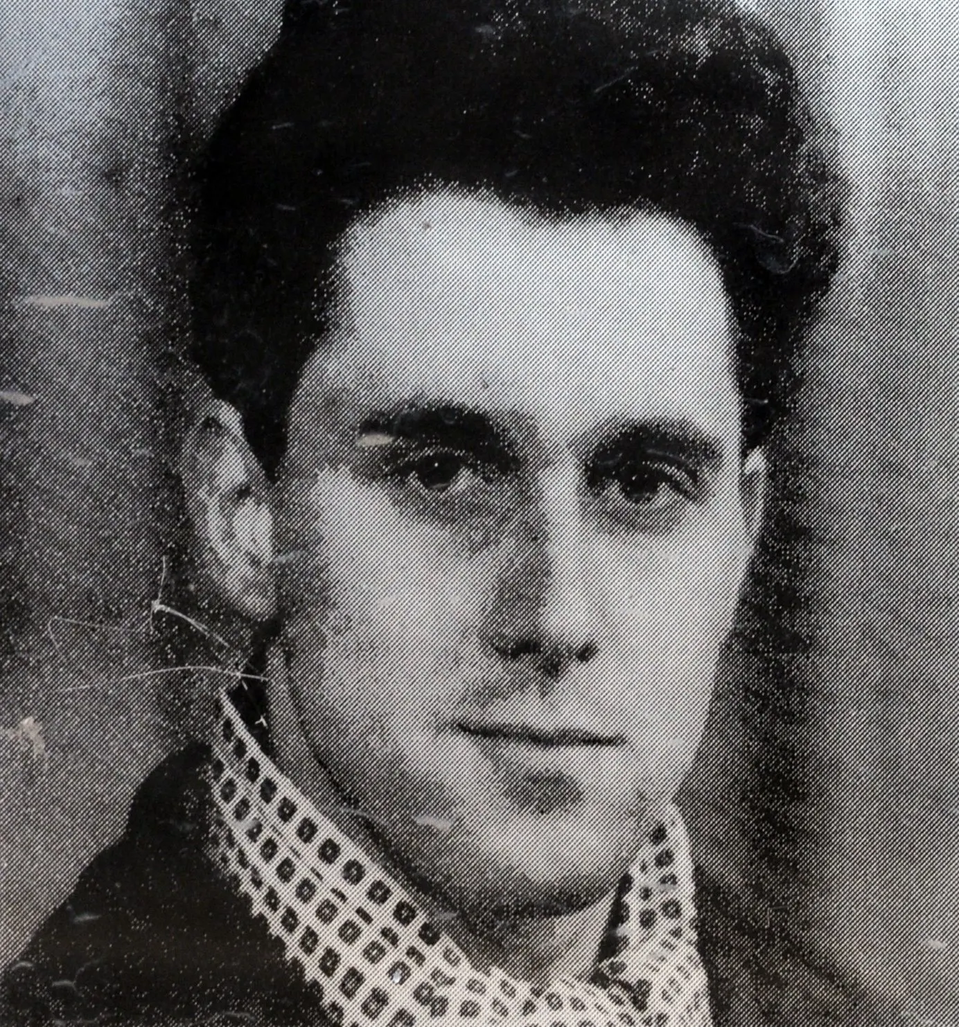 Black-and-white head-and-shoulders photograph of a young dark-haired man in a patterned shirt