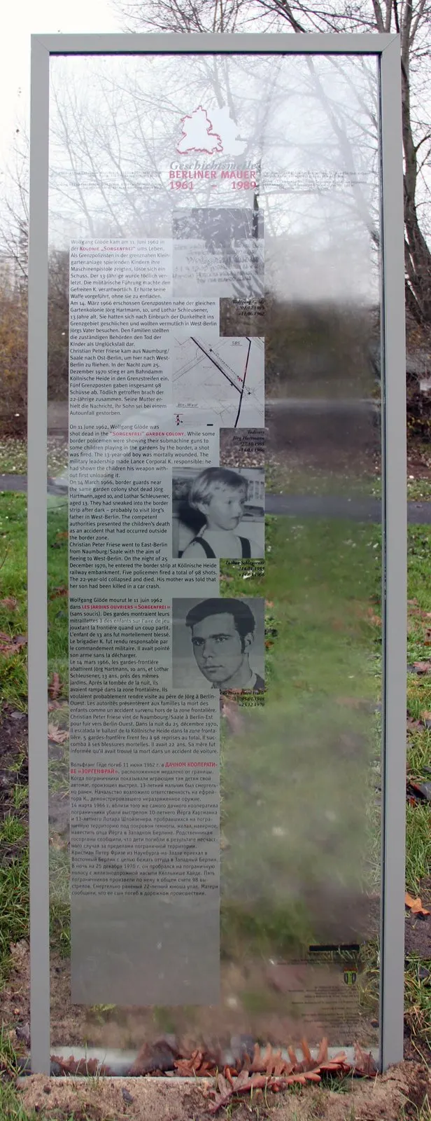 Tall glass panel in a steel frame with text in several languages, a map and black-and-white photographs, in a park