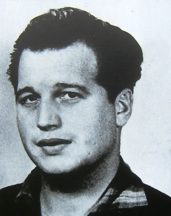 Black-and-white head-and-shoulders photograph of a young man with dark swept-back hair and an open-necked patterned shirt