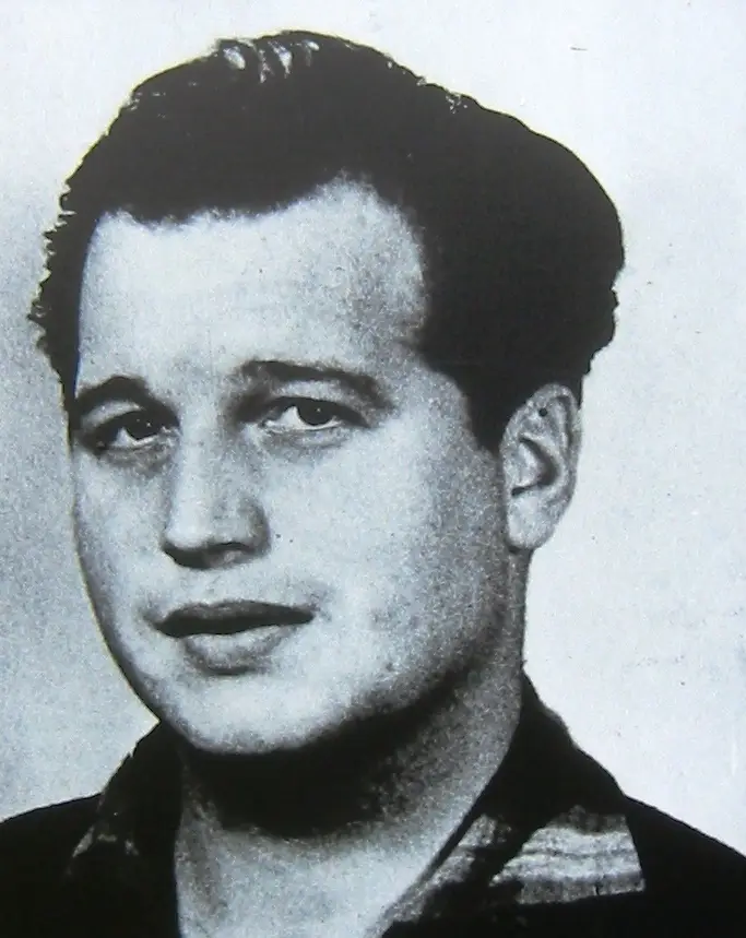Black-and-white head-and-shoulders photograph of a young man with dark swept-back hair and an open-necked patterned shirt