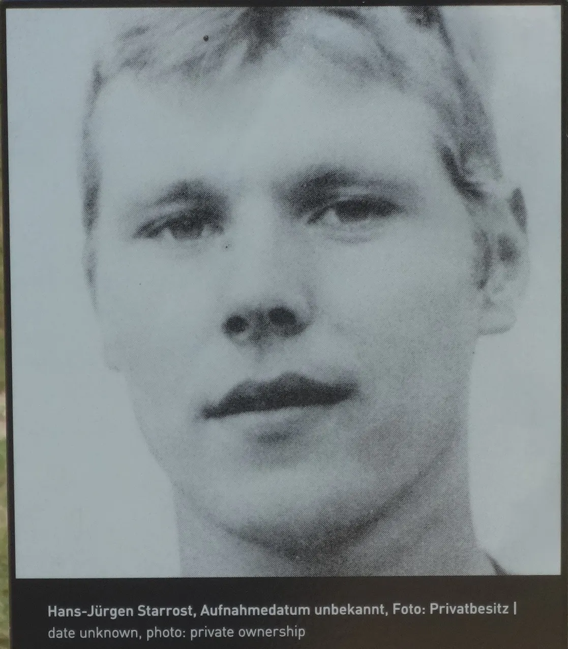 Black-and-white close-up portrait of a young man with short fair hair, with a caption strip below