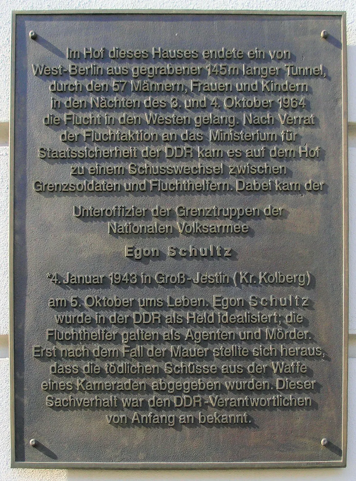 Bronze plaque on a wall with raised text about the escape tunnel and the death of border soldier Egon Schultz