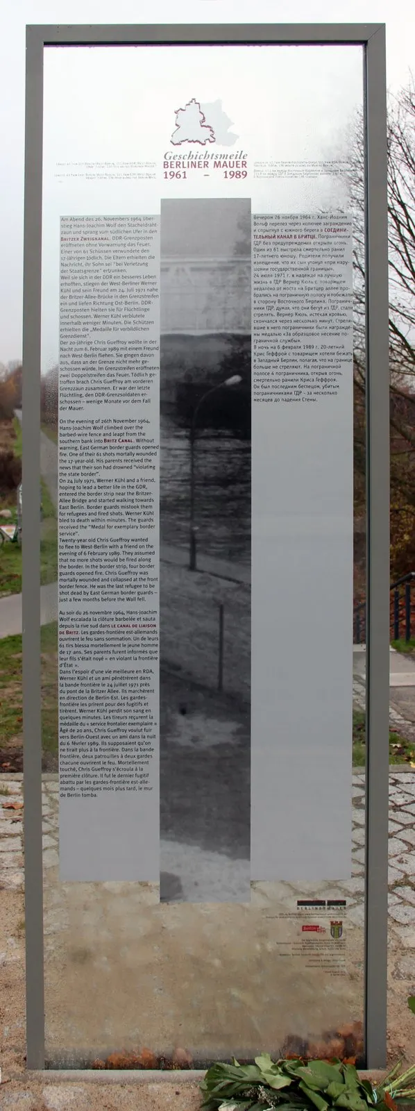Glass panel with multilingual printed text and a black-and-white image of the border strip, flowers at its foot