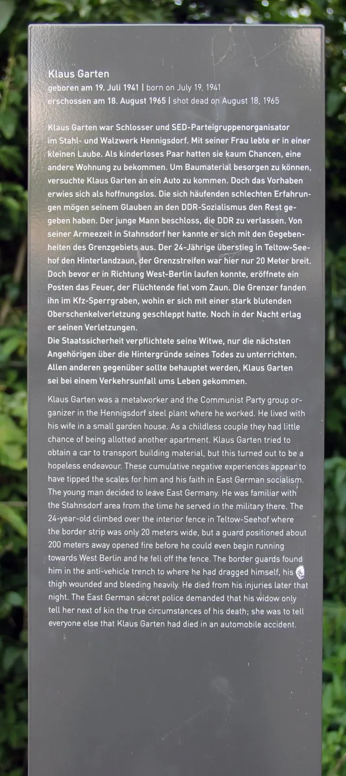 Dark grey panel with white text in German and English headed "Klaus Garten", in front of green foliage