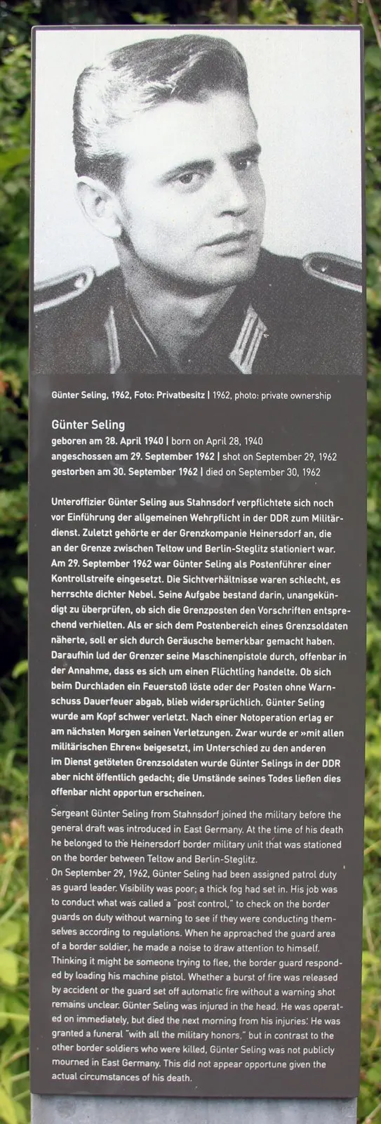 Grey stele with his portrait at the top and German and English text below