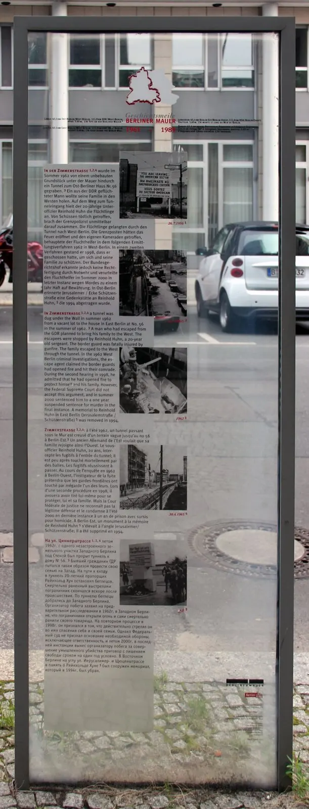Glass panel in a steel frame with text and small historical photos, street behind