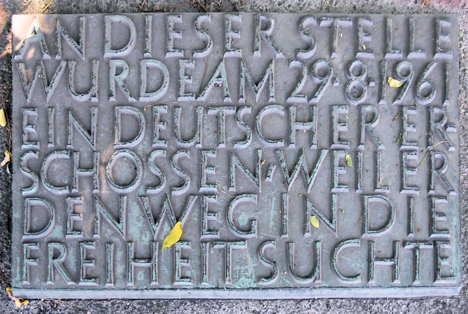 Weathered bronze plaque reading "An dieser Stelle wurde am 29.8.1961 ein Deutscher erschossen, weil er den Weg in die Freiheit suchte"