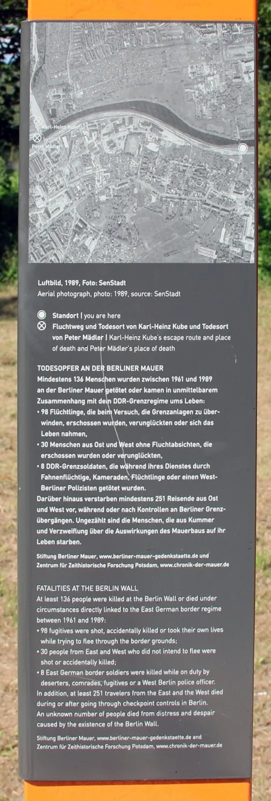 Panel with a black-and-white aerial photograph of a canal and town with two labelled marks, above German and English text