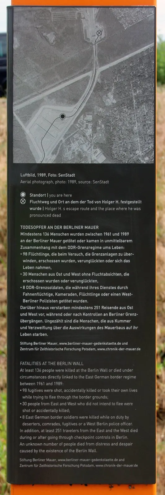 Dark information panel on an orange column with an aerial photograph of roads and a checkpoint, a route line and circled markers