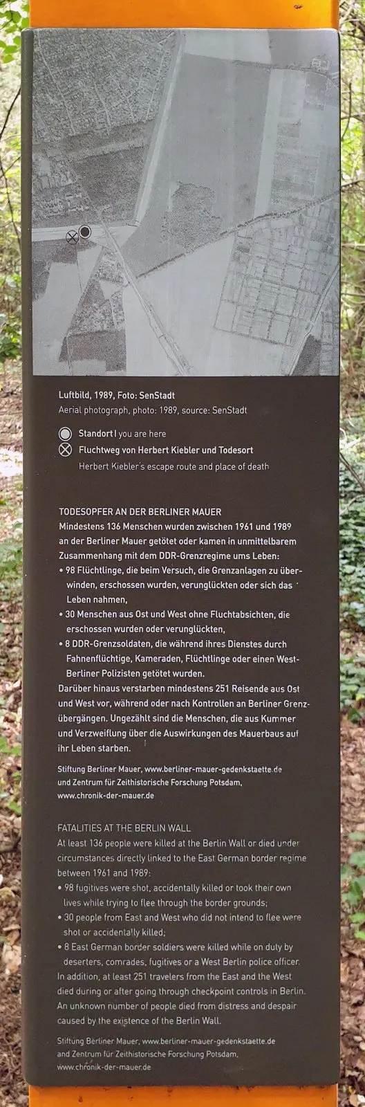Panel with a black-and-white aerial photograph marked with two symbols, above German and English text