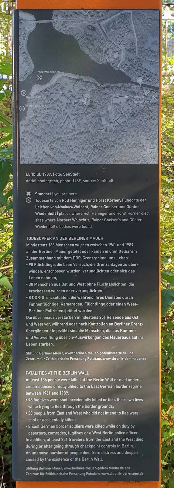 Panel with a black-and-white aerial photograph of a park and lake shore with labelled marks, above German and English text