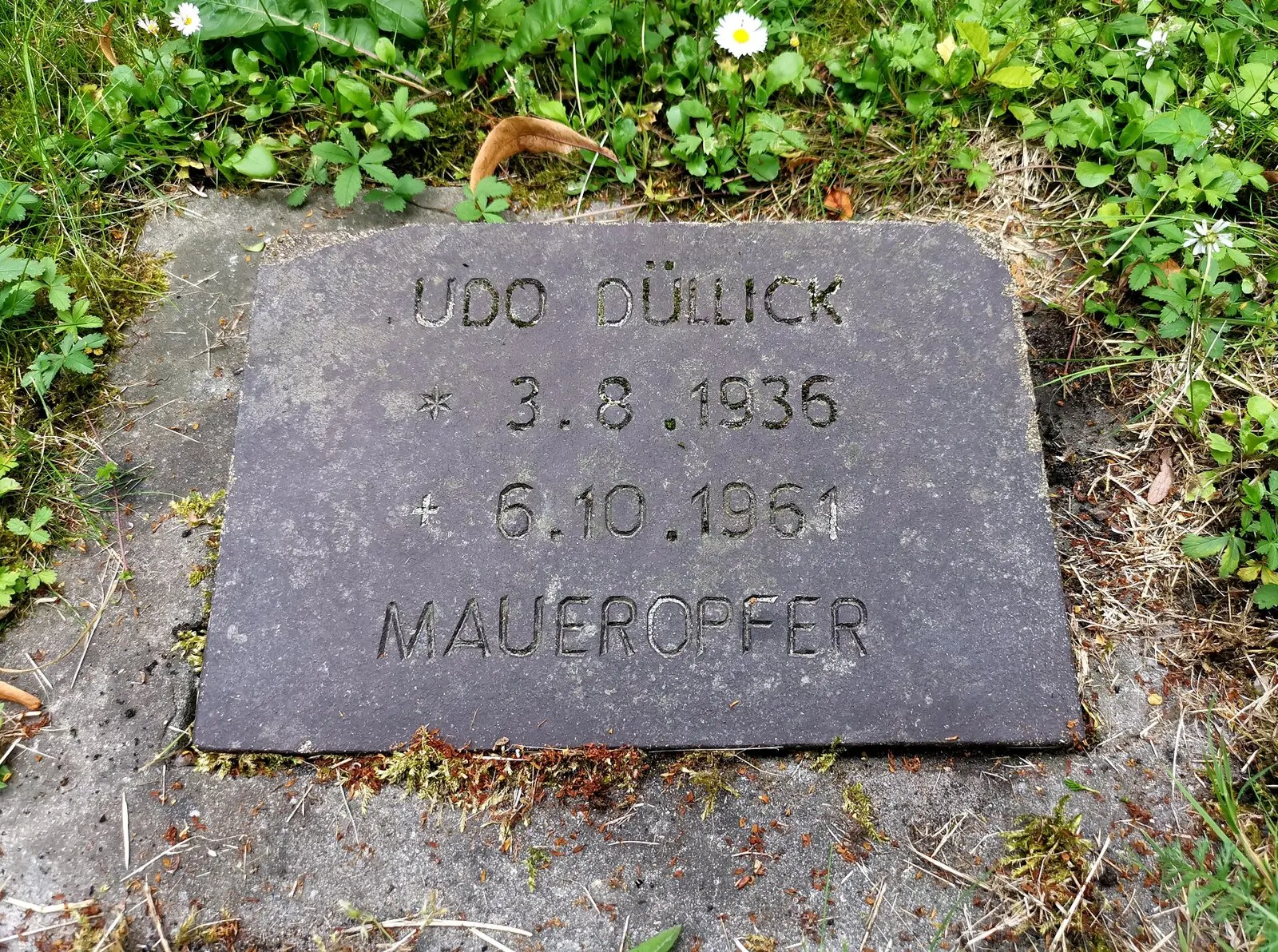 Dark grave plate among clover inscribed "Udo Düllick * 3.8.1936 † 6.10.1961 Maueropfer"
