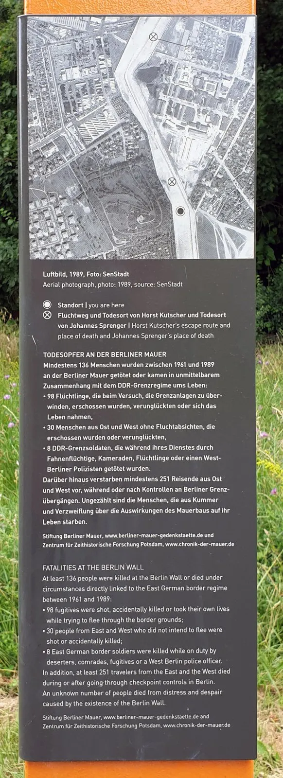 Dark information panel on an orange column with an aerial photograph of the border strip and buildings, marked with circled crosses