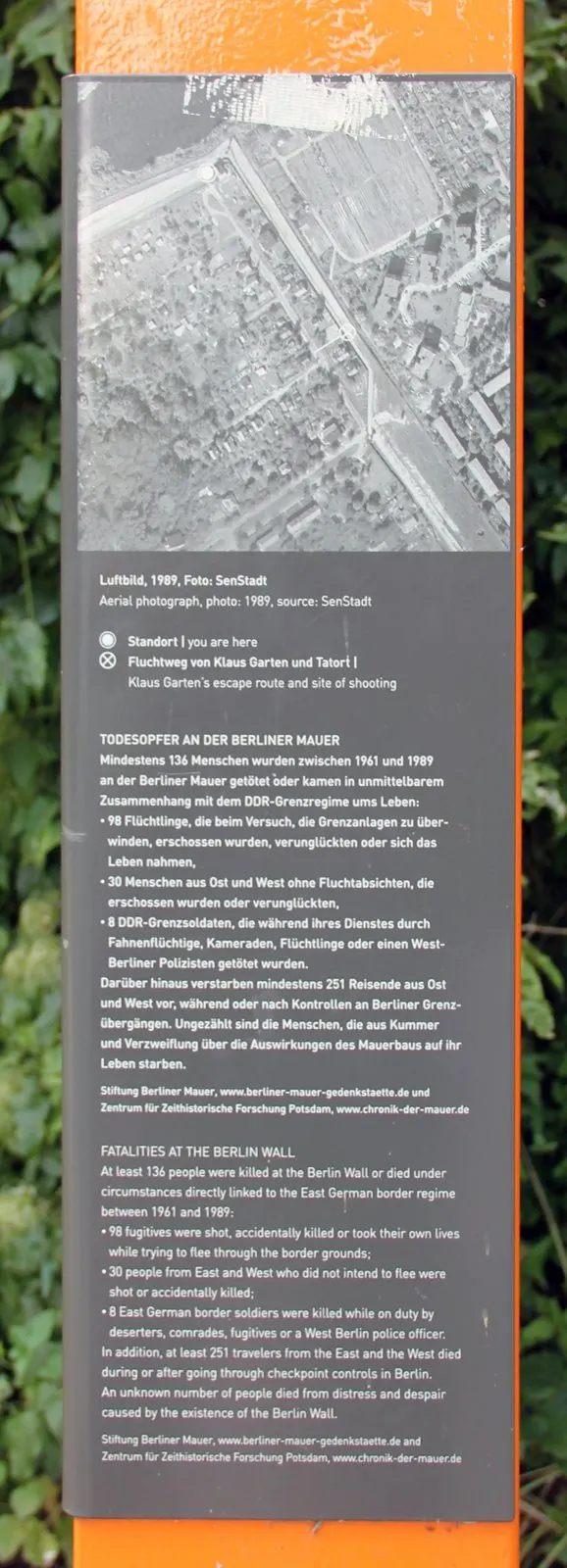 Panel on an orange column with a black-and-white aerial photograph of streets and gardens, above German and English text