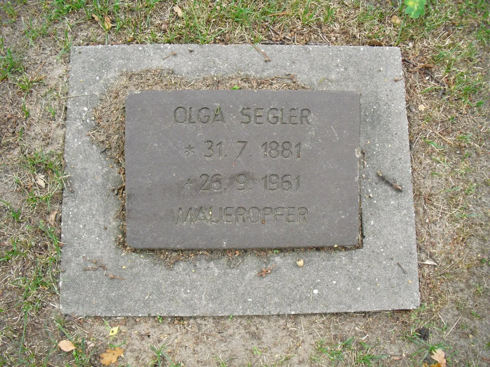 Dark plate set in concrete in grass inscribed "Olga Segler 31.7.1881 26.9.1961 Maueropfer"