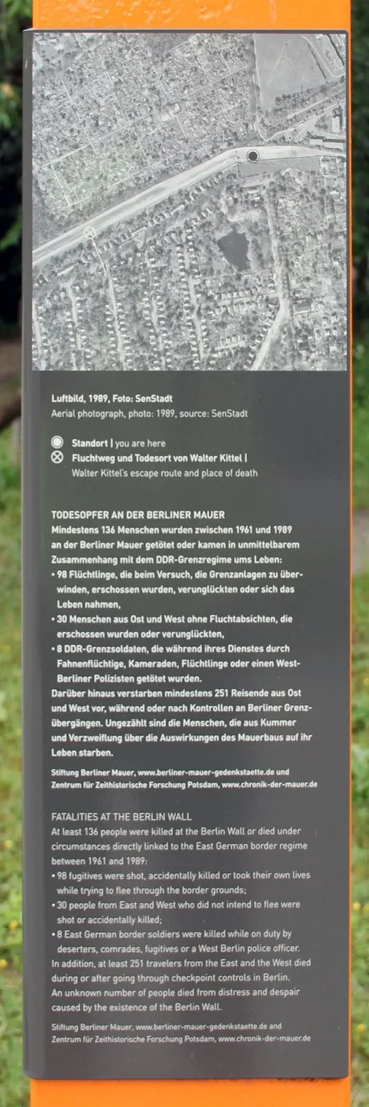 Panel on an orange column with a black-and-white aerial photograph of a residential area and the border strip, above German and English text