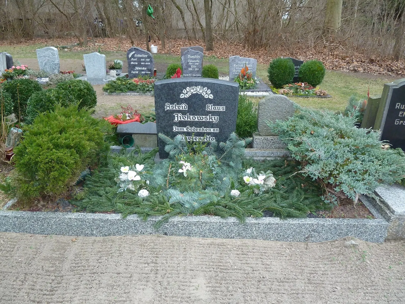 Dark granite headstone with family names and a line of remembrance, in a grave planted with evergreens and white flowers