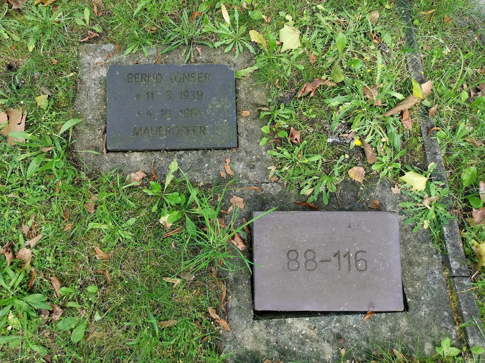Dark grave plate in grass inscribed "Bernd Lünser … Maueropfer", with a numbered plate "88-116" beside it