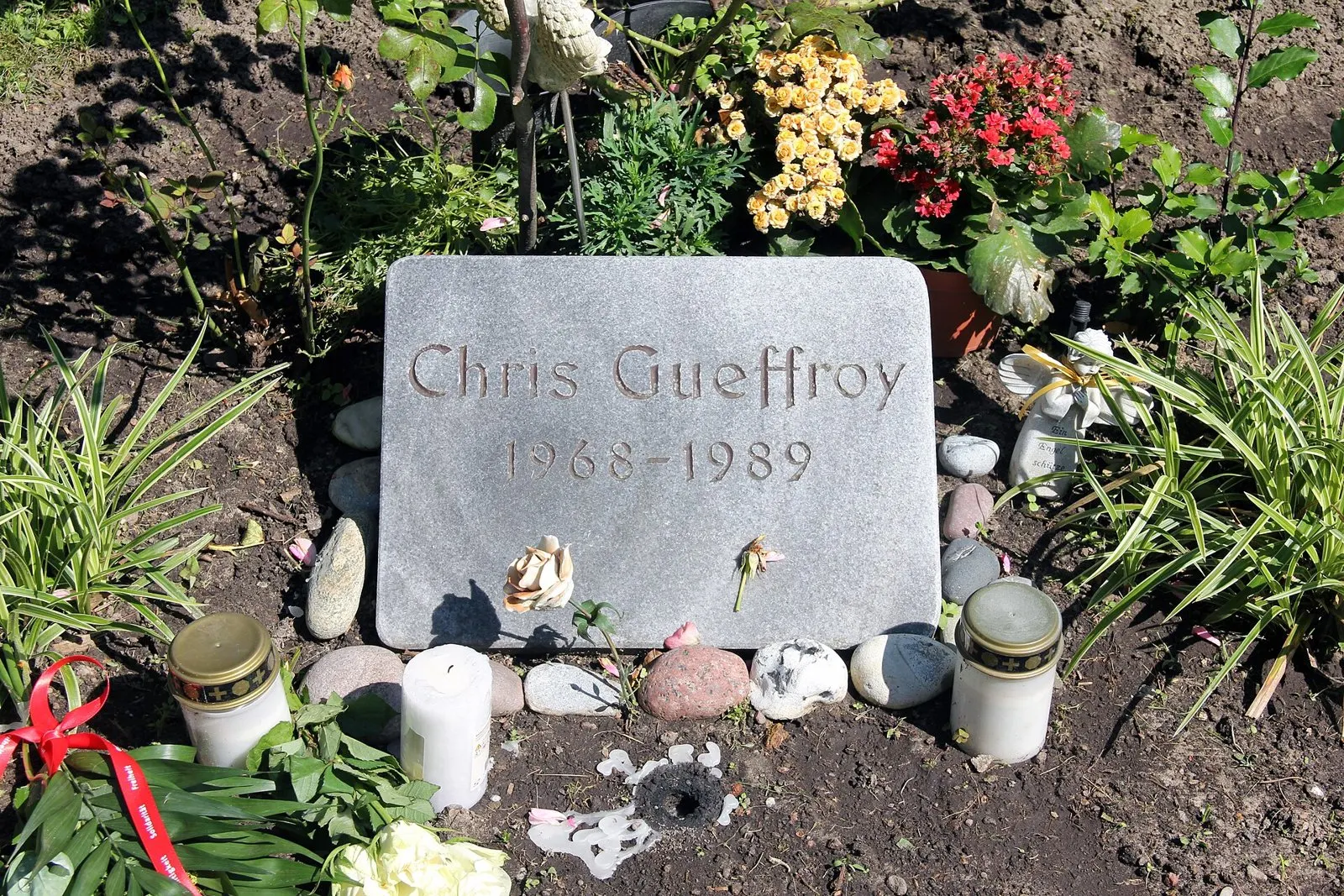 Grey stone slab reading "Chris Gueffroy 1968–1989" surrounded by flowers, candles and pebbles